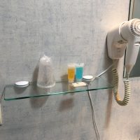 Ablage im Bad mit Zahnputzbechern, Shampoo und Seife. Daneben hängt ein Fön