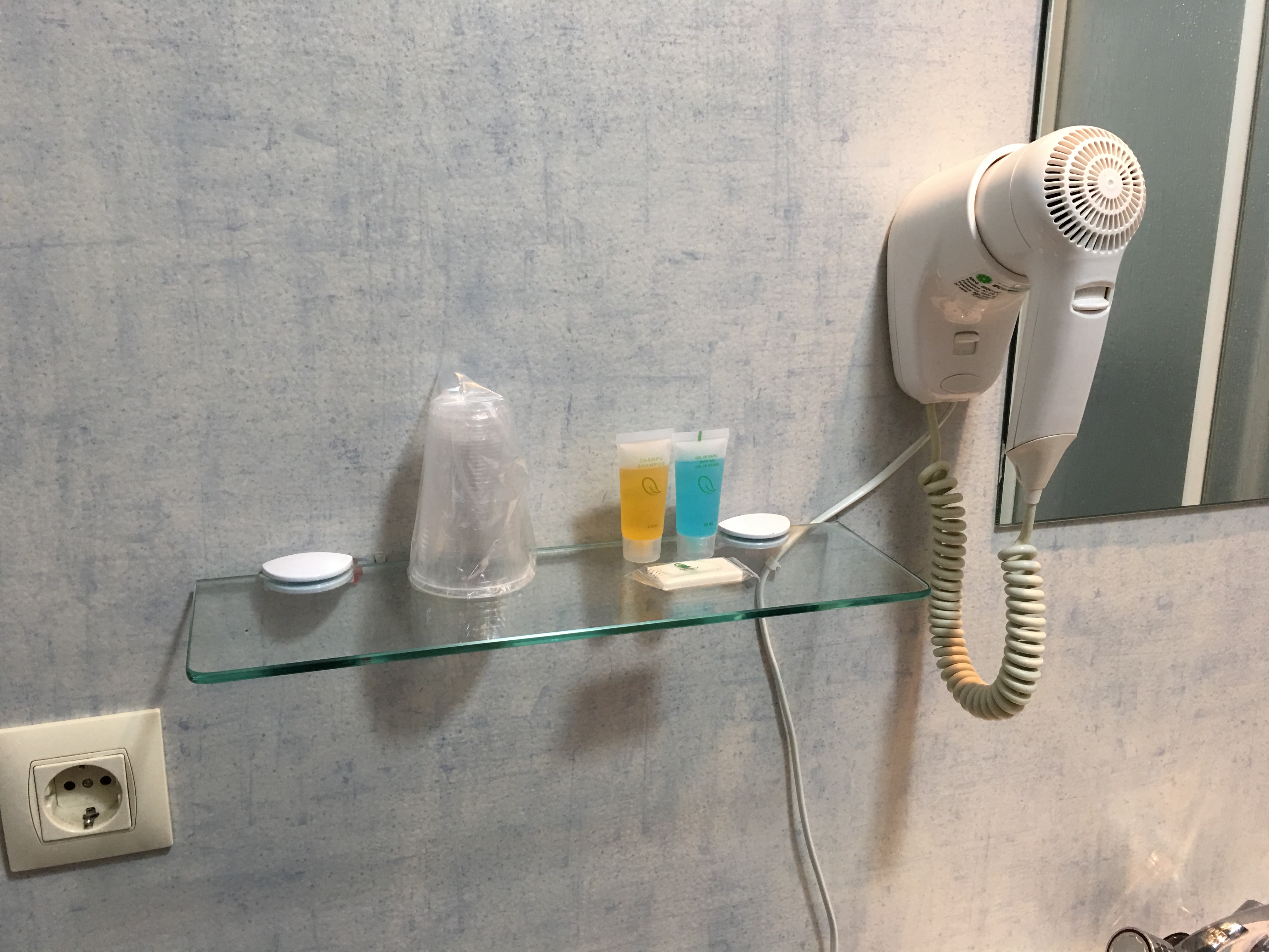 Ablage im Bad mit Zahnputzbechern, Shampoo und Seife. Daneben hängt ein Fön
