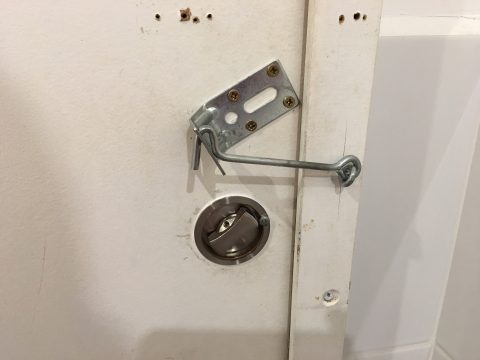 Improvisierter Riegel an einer Toilettentür. Man sieht anhand der Schraubenlöcher, dass es schon andere Verriegelungen gab.